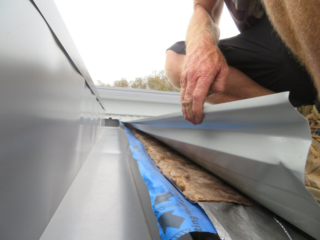 Building inspector in Hobart checking roof gutter for hidden defects and insulation issues
